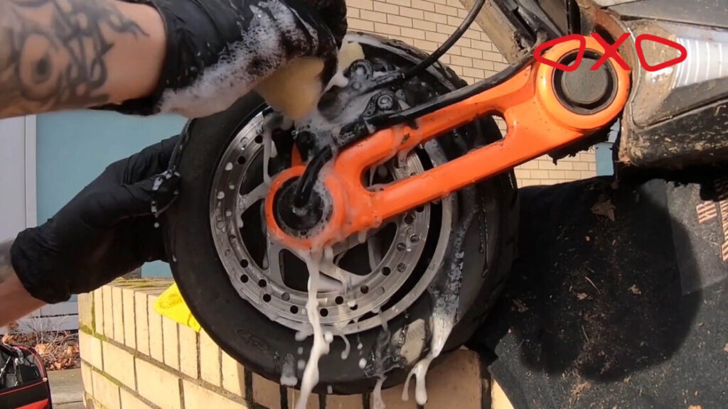 A man washes a wheel and tire of an electric scooter with a soapy sponge
