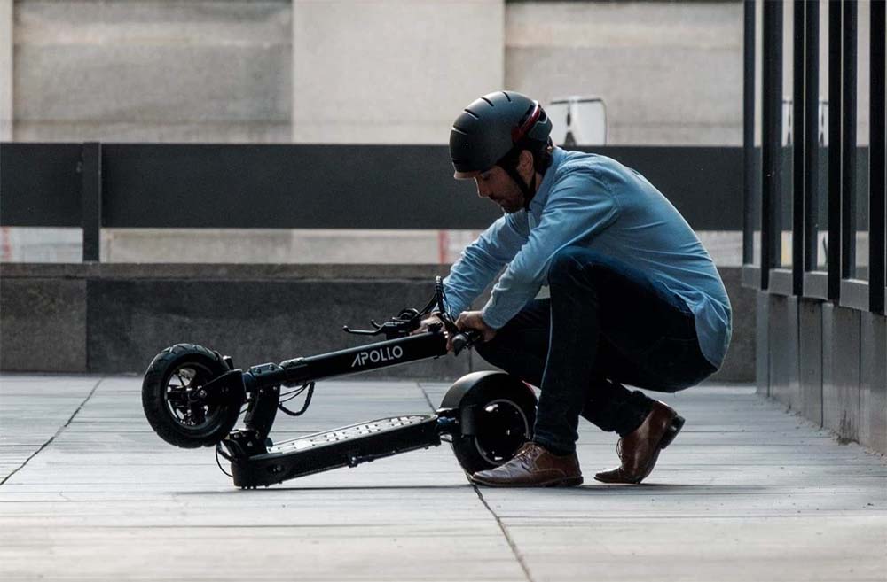 A man is folding up an Apollo Explore electric scooter