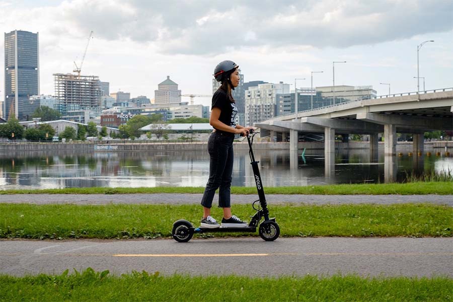 A women with a helmet is riding with an Apollo electric scooter