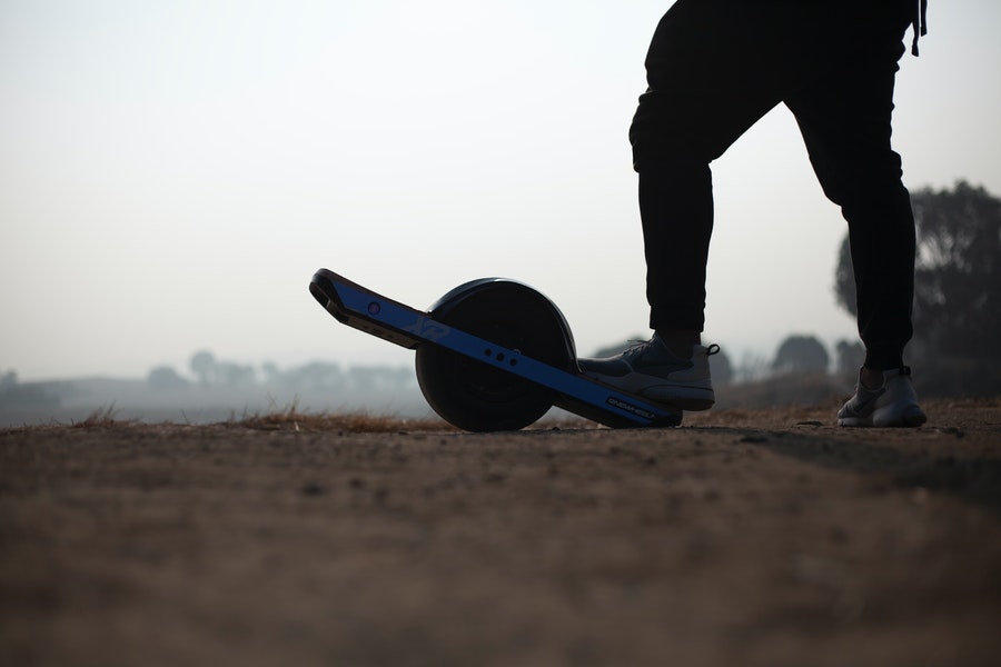 A man is standing next to the OneWheel hoverboard.
