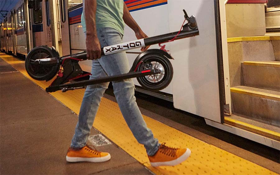 Man holding a Gotrax electric scooter while entering the train