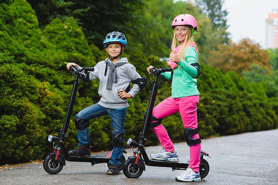 kid wearing the safety gear posing next to their electric scooters