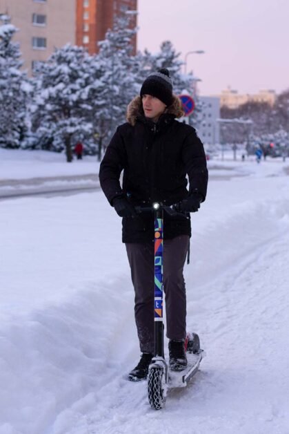 A man is riding with an electric winter scooter on a snowy street.