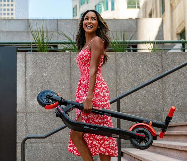 Woman in a dress carrying a folded Ninebot scooter