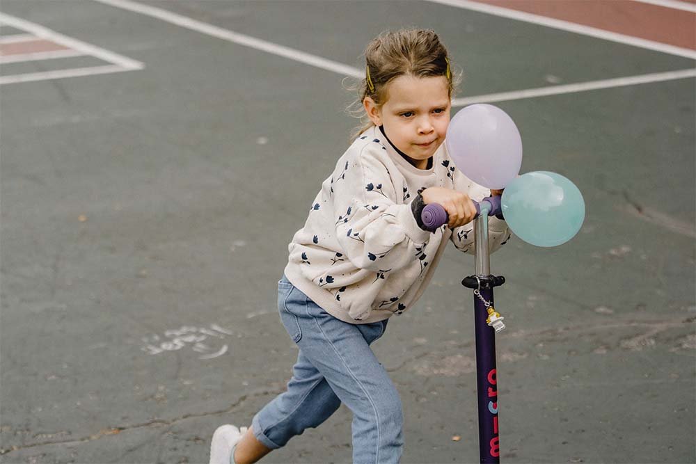 A small girl is riding with scooter.