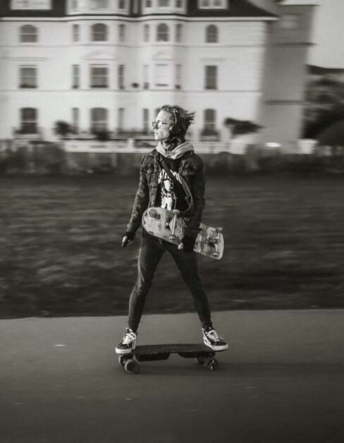 guy rides with electric skateboard and holds another skateboard under his arm