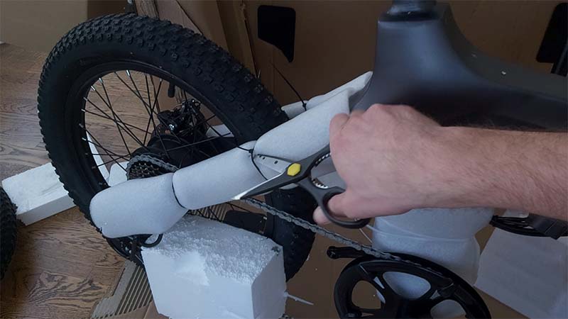 Cutting a strap that is holding a softening cushion around an e-bike.
