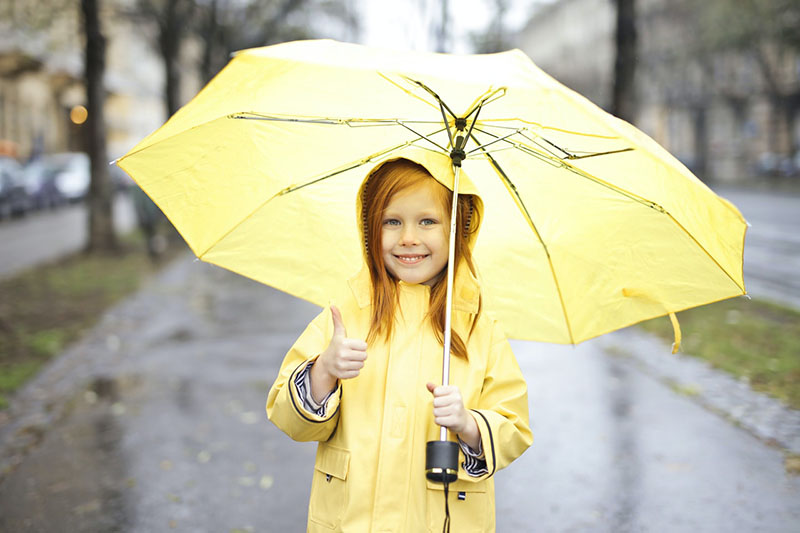 Small girl in yellow raincoat with yellow umbrella