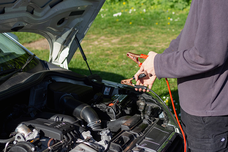 man holding a jumpstart cables in front of the car