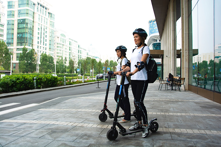 women with helmets riding electric scooters in the city